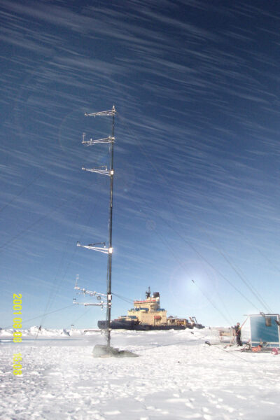 EX telescopic mast fully erected on Antarctic sea ice with meteorological instruments and weather sensors, with a research icebreaker visible in the background.