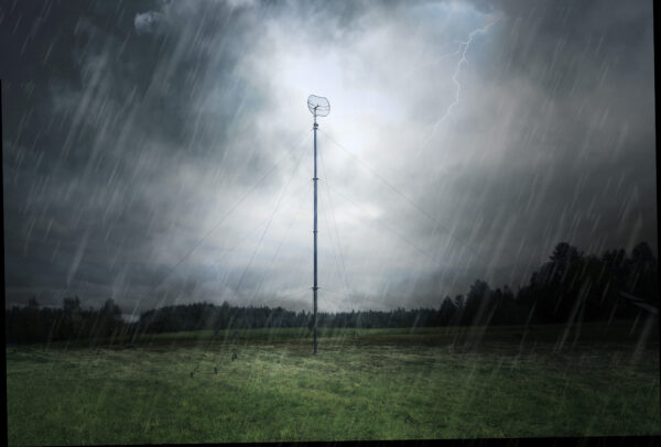 EX telescopic mast fully erected with a parabolic grid antenna in a grass field during a heavy thunderstorm, with rain falling and lightning visible in dark storm clouds.