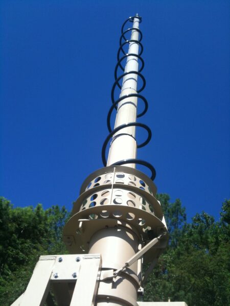 EXB telescopic mast fully extended against a clear blue sky, viewed from below, with stay-rope guy ring at the base for stable outdoor deployment.